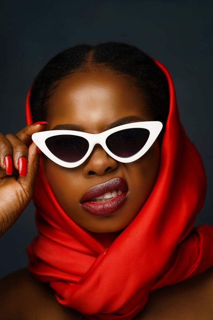 portrait-of-a-young-woman-wearing-a-red-headscarf-and-sunglasses-12008355 Stylish woman posing with red headscarf and white sunglasses in studio setting.