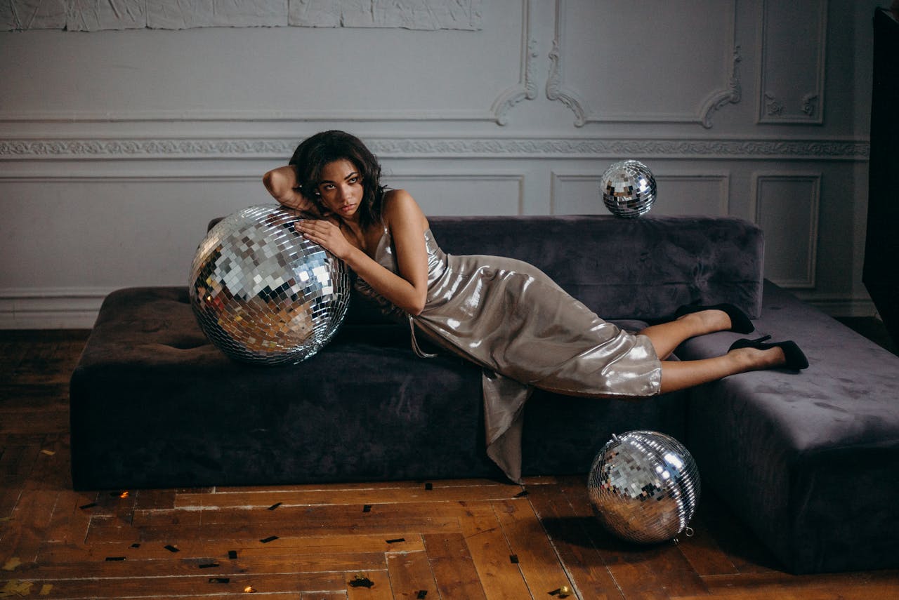 Elegant fashion model lying on a couch with disco balls in a stylish indoor setting.